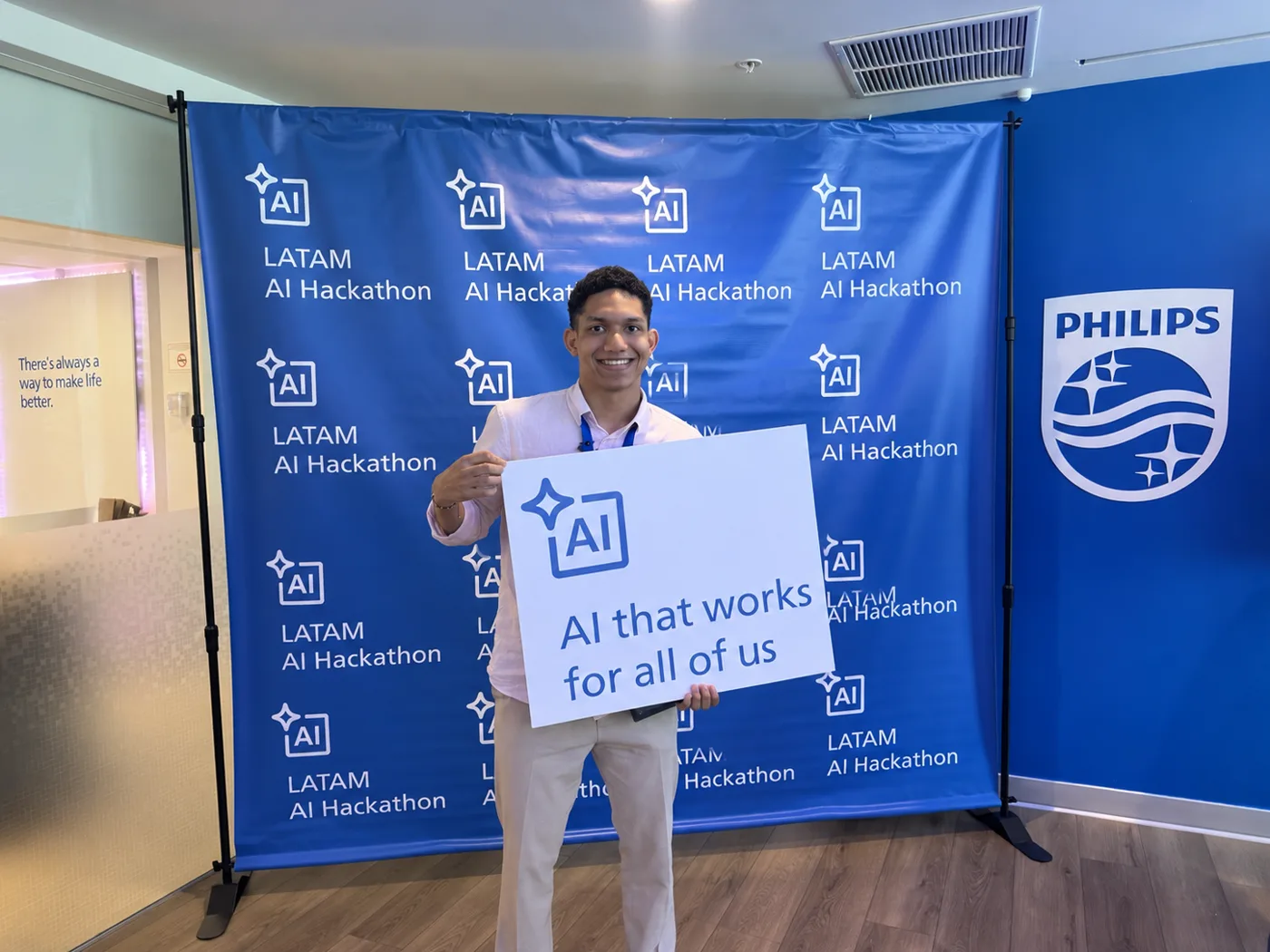 Tincho con el letrero AI that works for all of us frente al telón del LATAM AI Hackathon